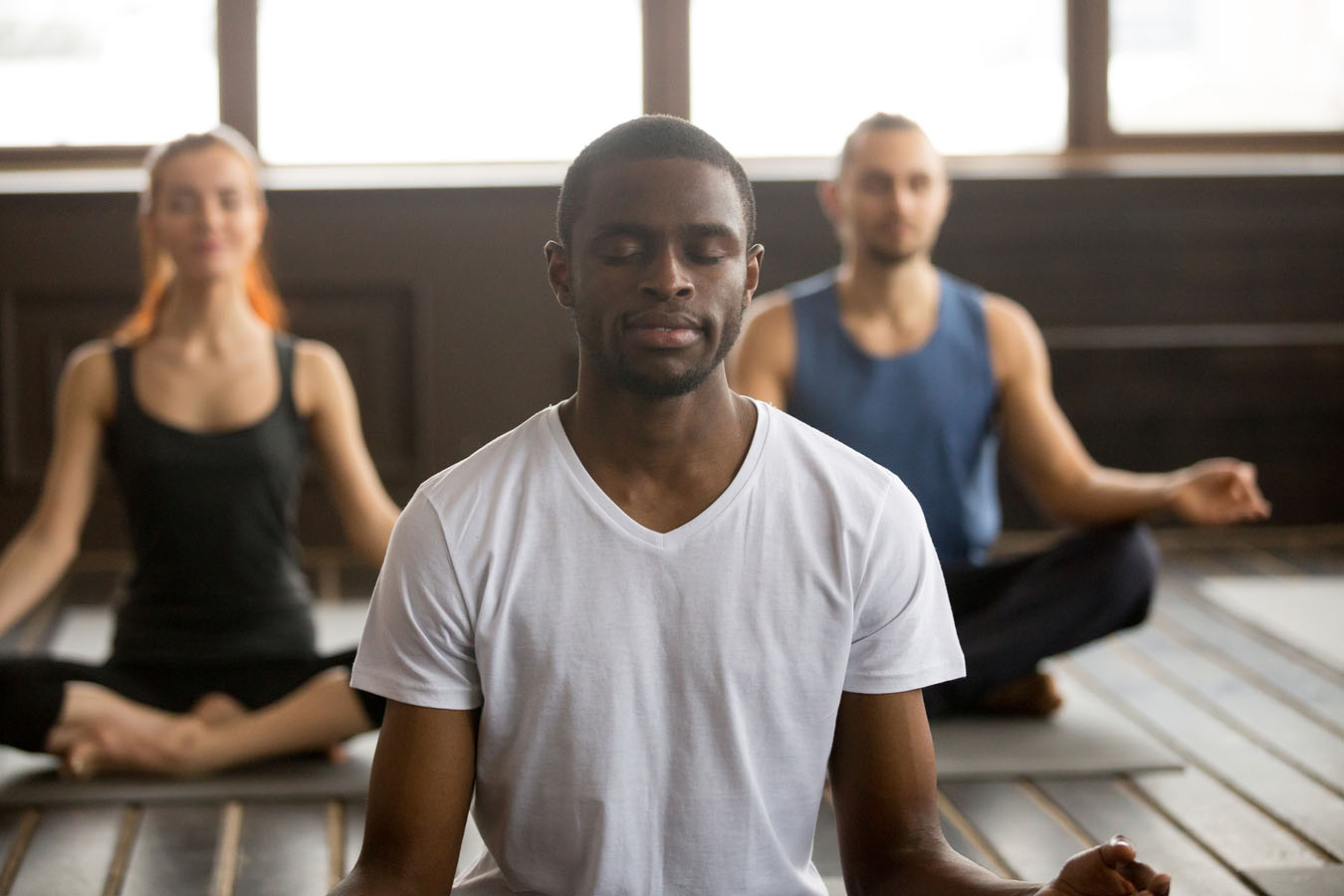 Young black man and a group of sporty people practicing yoga lesson with instructor, sitting in Sukhasana exercise, Easy Seat pose with mudra gesture, students training in club, working out, close up